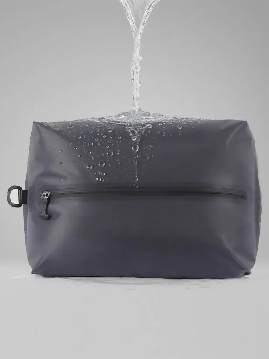 Roll-top dry bag with a sealed closure lying beside wet angling gear on a gravel bank after rain