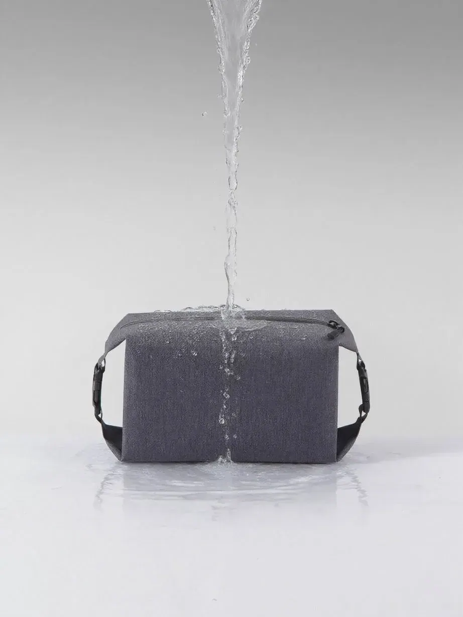 Roll-top dry bag lying half packed on firm damp sand with its top folded down three turns and a reel pouch tucked alongside