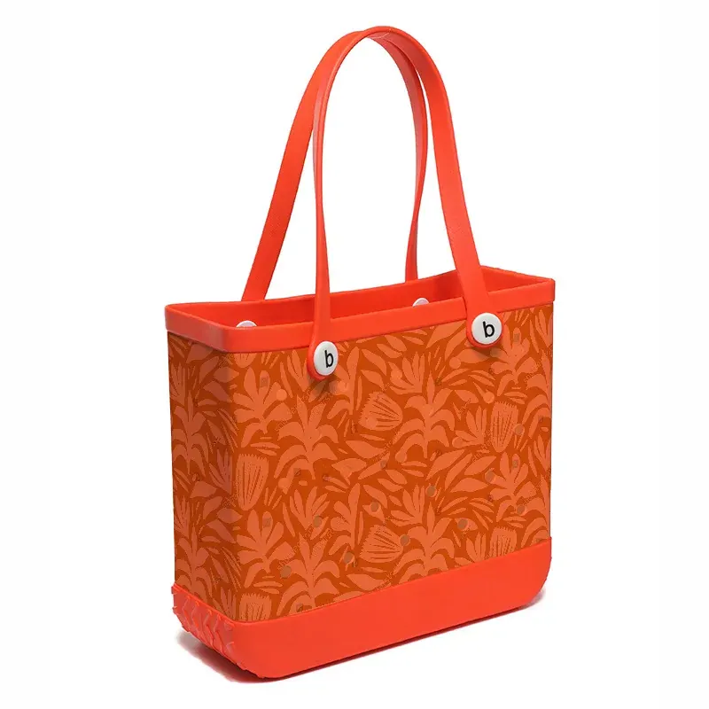 Perforated EVA beach tote packed with towels and bottles standing level on sand with the rim held open