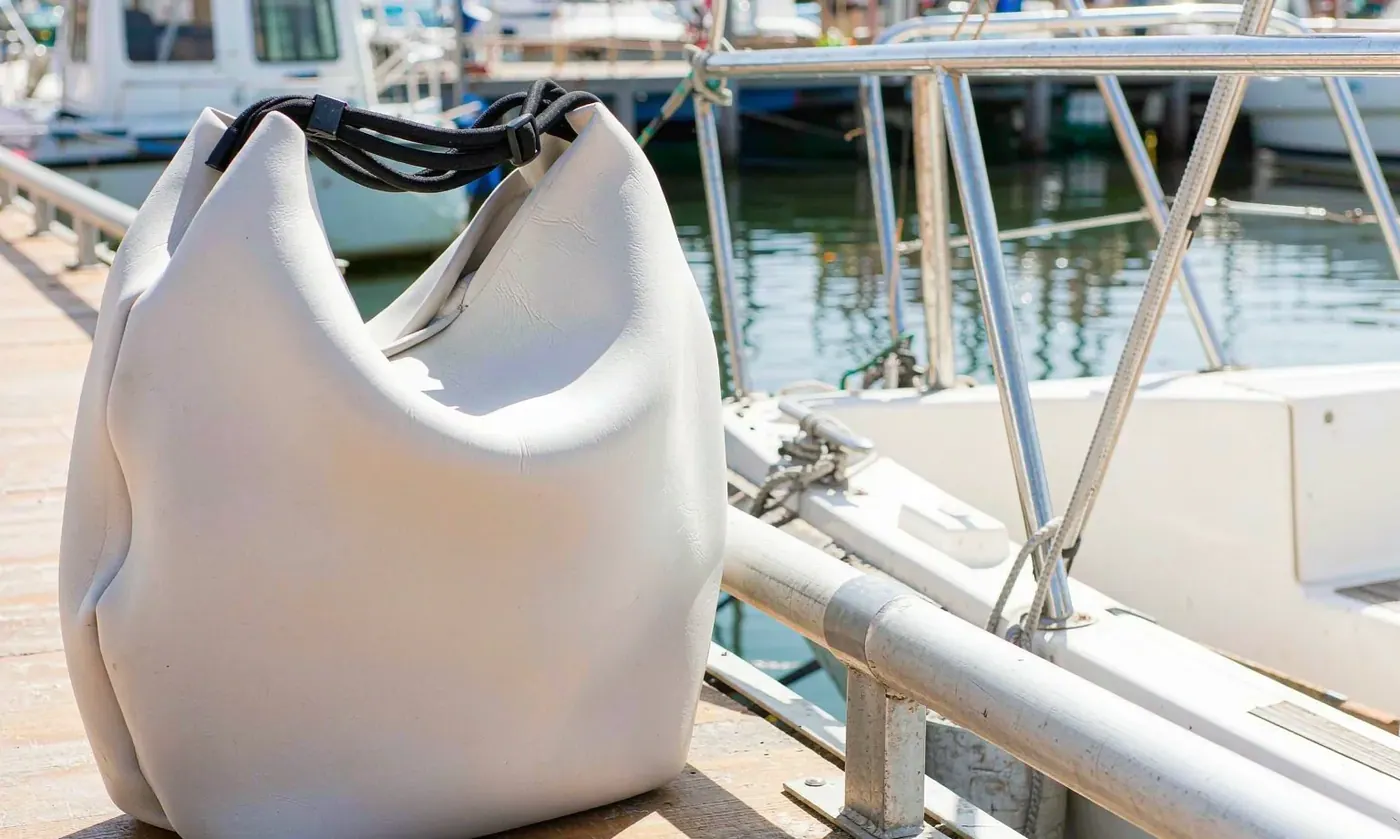 Perforated EVA tote standing on a marina pontoon beside mooring lines with bottles upright inside