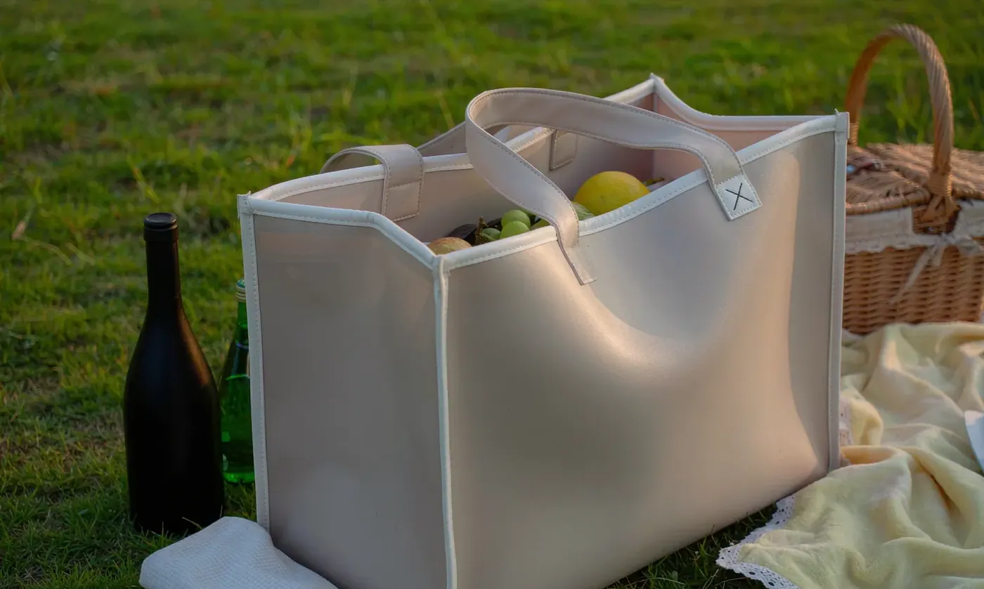 Perforated EVA tote standing upright on grass at a picnic holding bottles and food containers without slumping