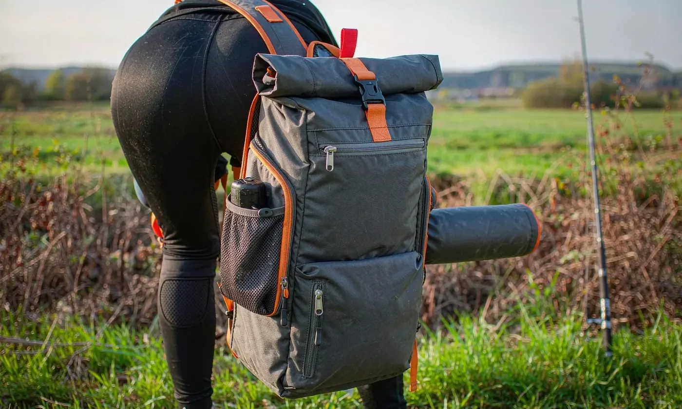 Angler wearing a compact fishing sling pack swung to the front while fishing from a low bank beside a river
