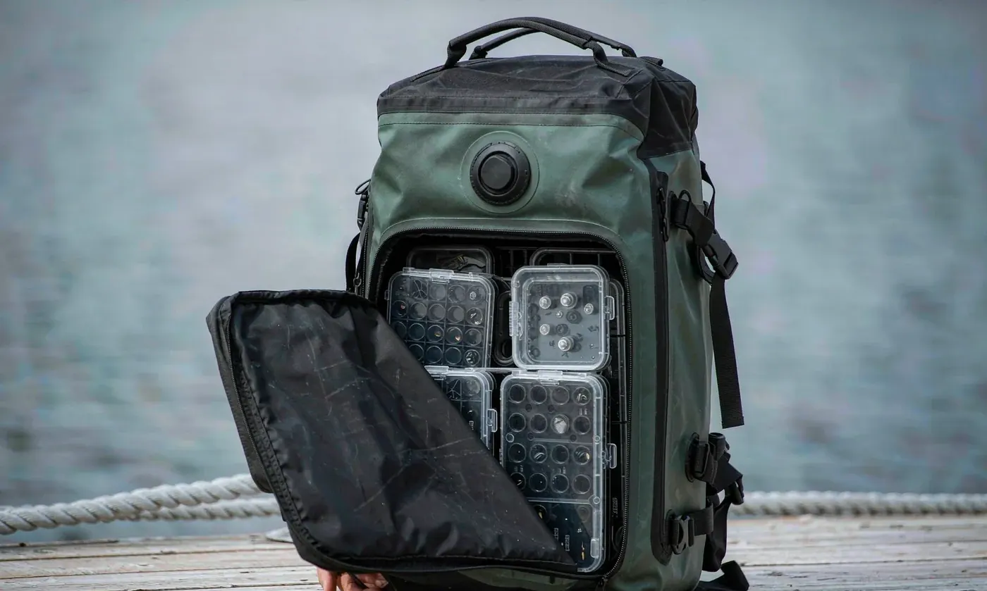 Fishing tackle backpack opened on a boat deck with stacked utility trays and tool pockets visible