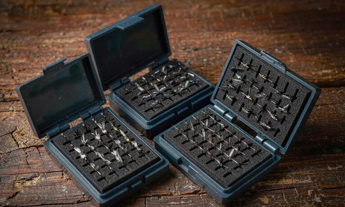 Waterproof fly boxes with rubber gasket seals opened close up beside a stream with wet flies inside