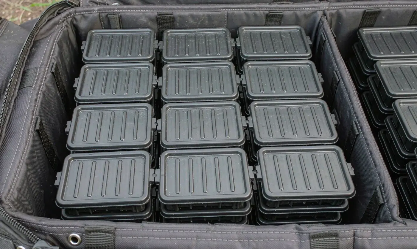 Four tackle trays stacked inside the open compartment of a fishing tote with dividers visible