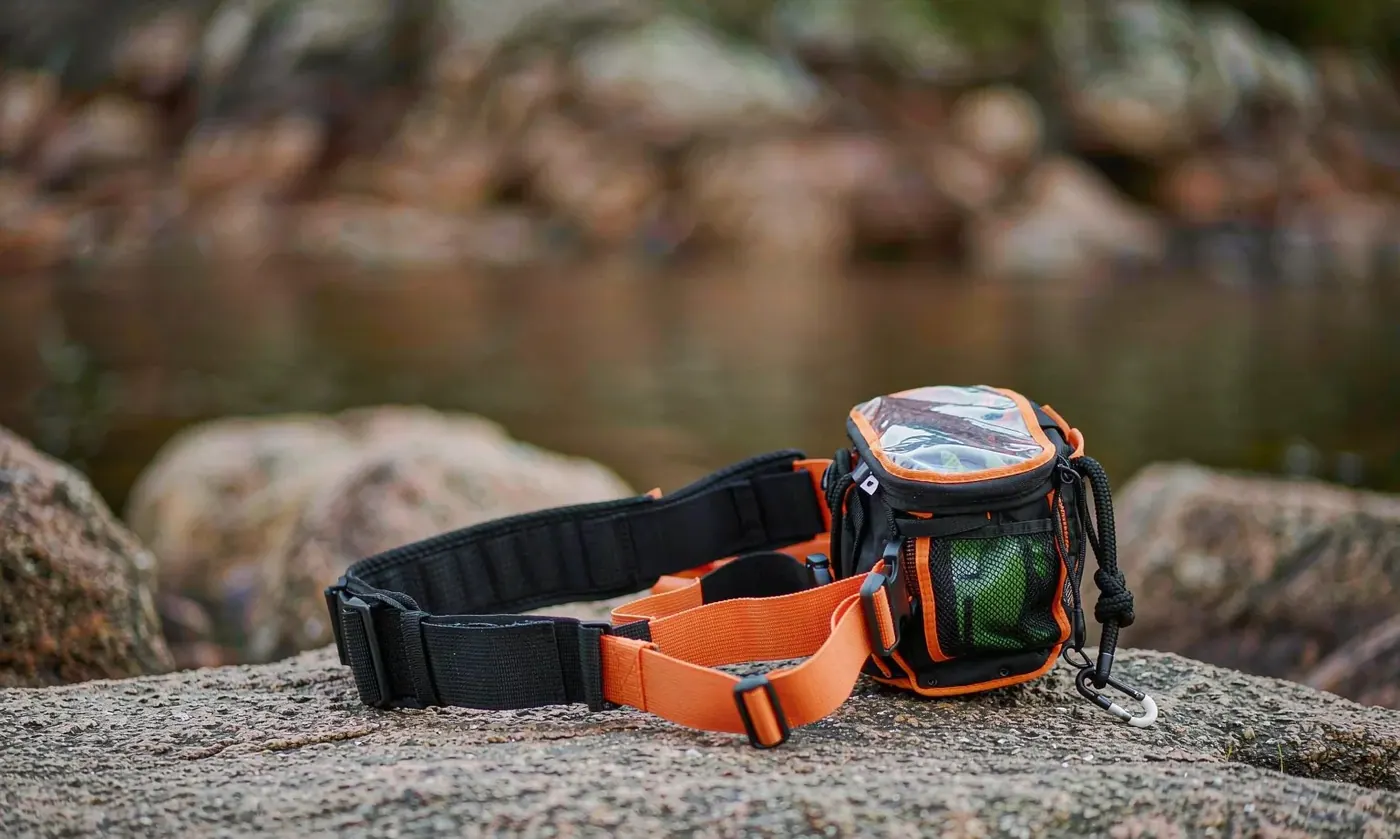 Waterproof wading belt pack worn at the waist in a shallow river, water beading into separate droplets across the outer face fabric