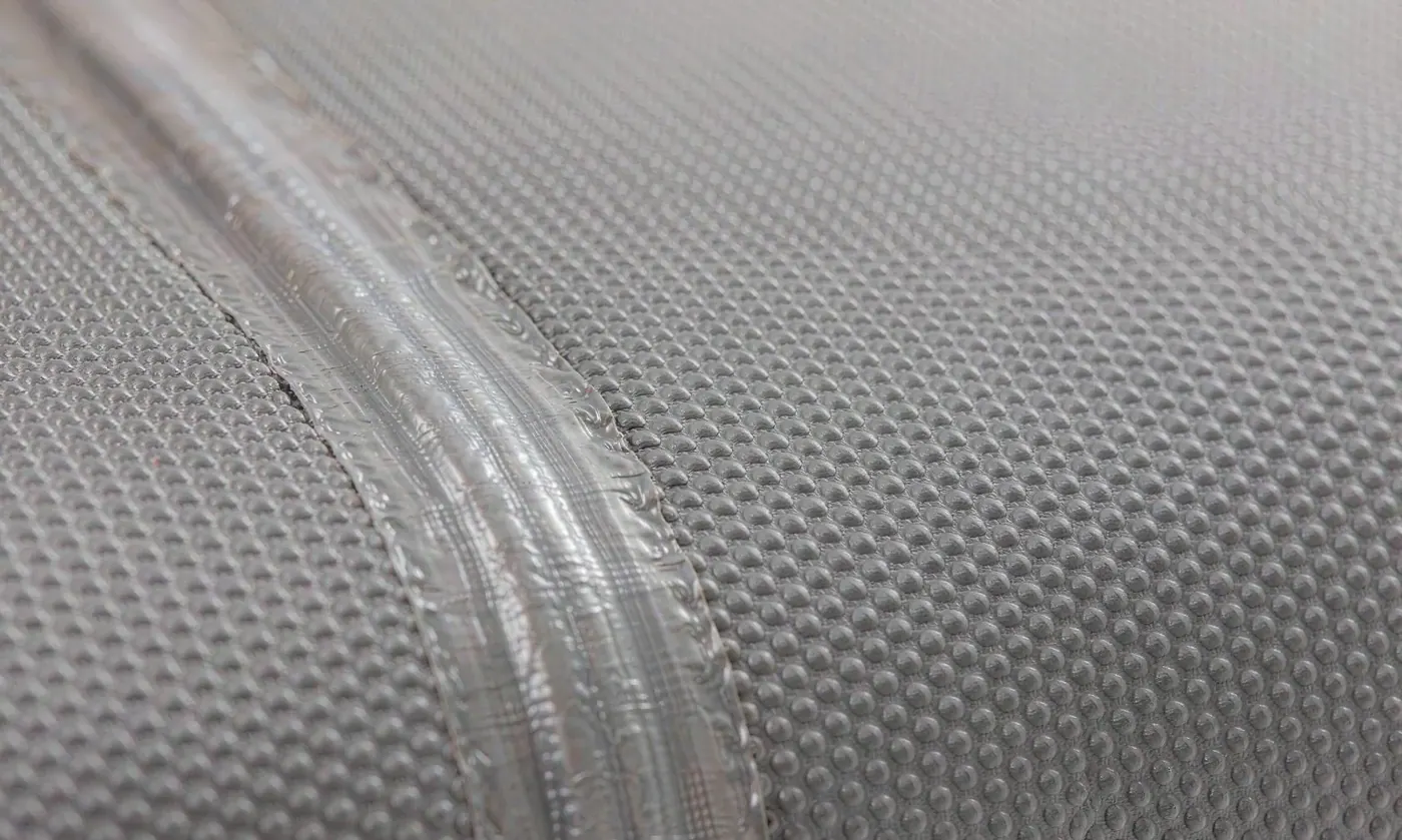 Close-up of a welded seam on a waterproof backpack panel showing the fused film band where two laminated edges have been melted into one continuous surface